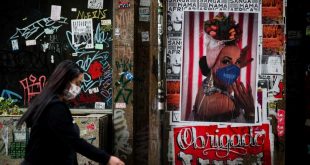 Una mujer con mascarilla caminando frente a un poster artístico en Sao Paulo.